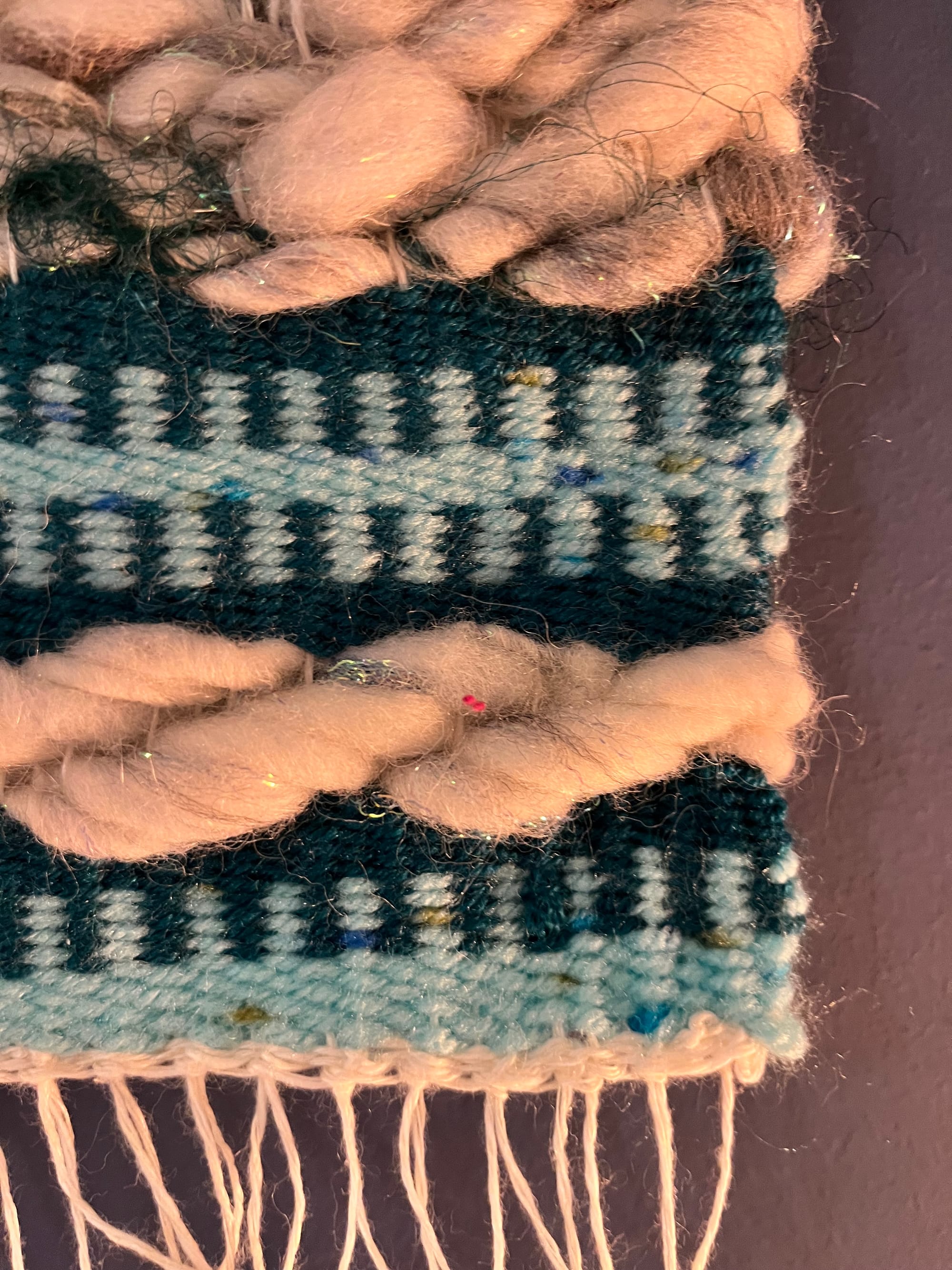 A detail of the larger piece, focusing on the bottom right corner. There is a thin white fringe along the bottom edge of the tapestry.